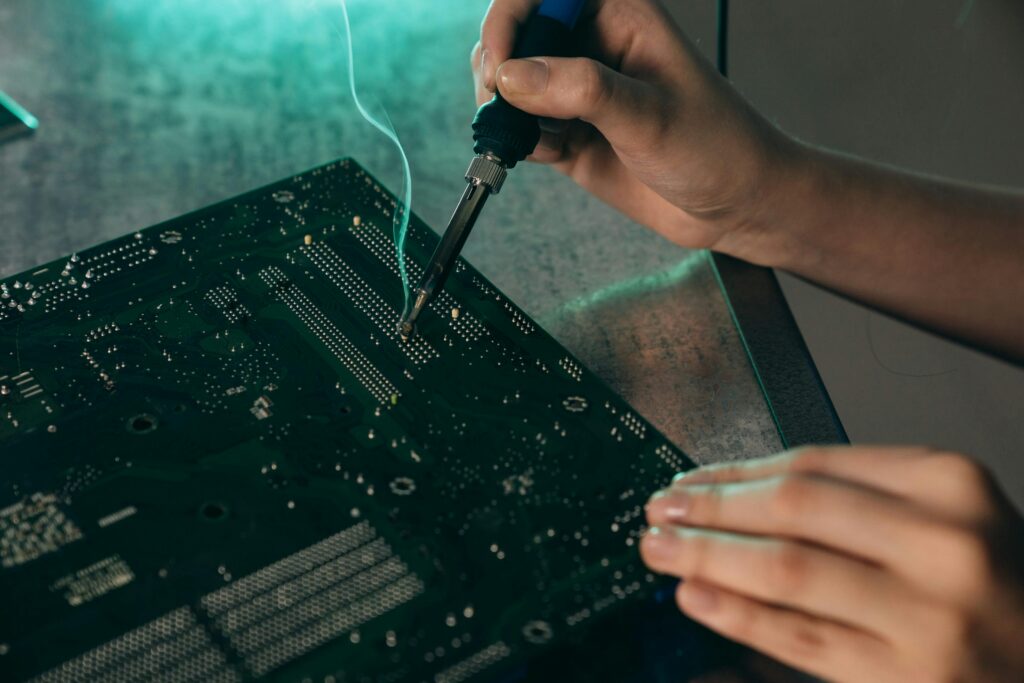 Close-up of hands soldering components on a motherboard with a soldering iron.